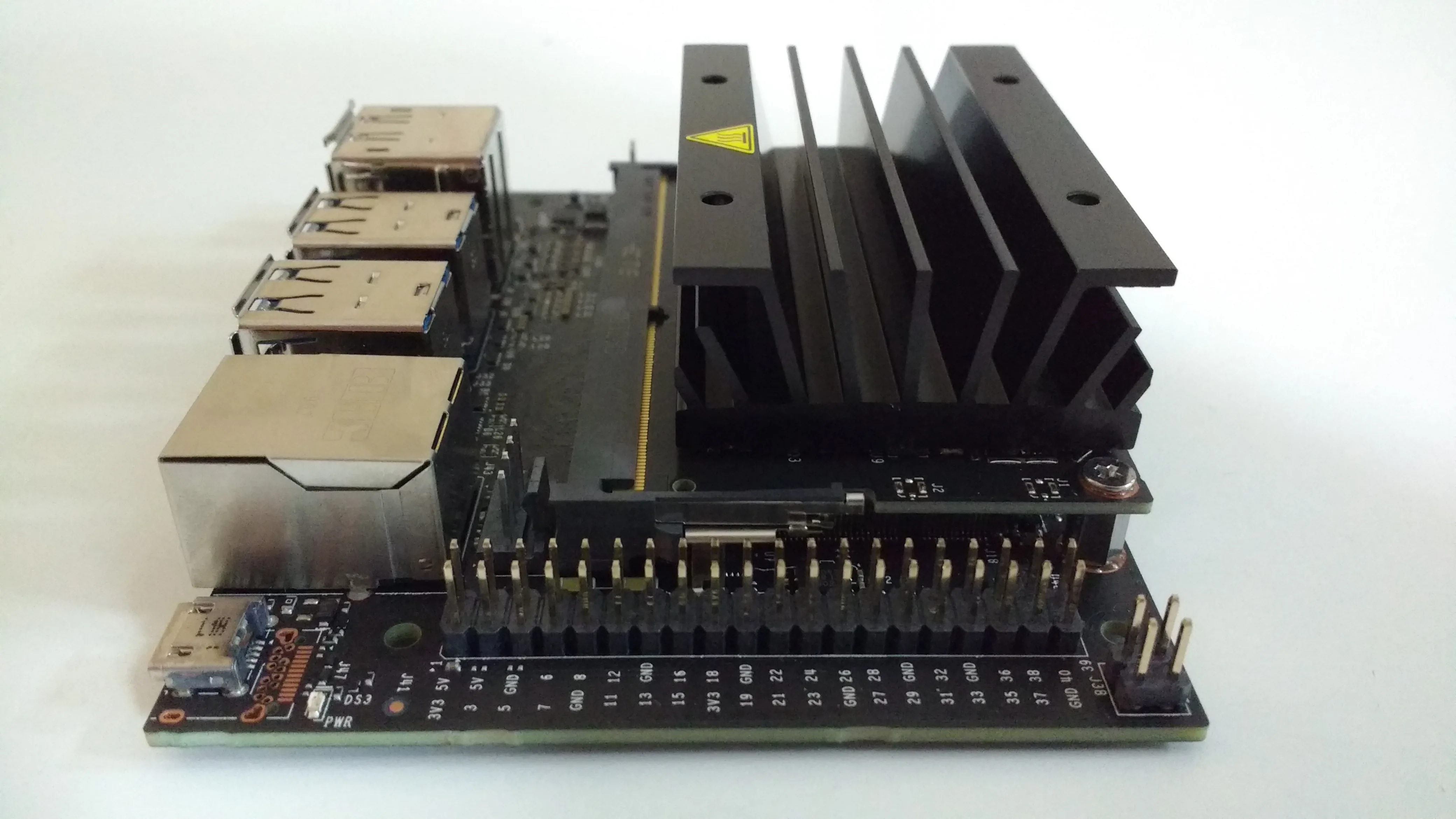 Close view of a Jetson Nano development board with a large finned heat sink, metal connection ports, and pin headers.