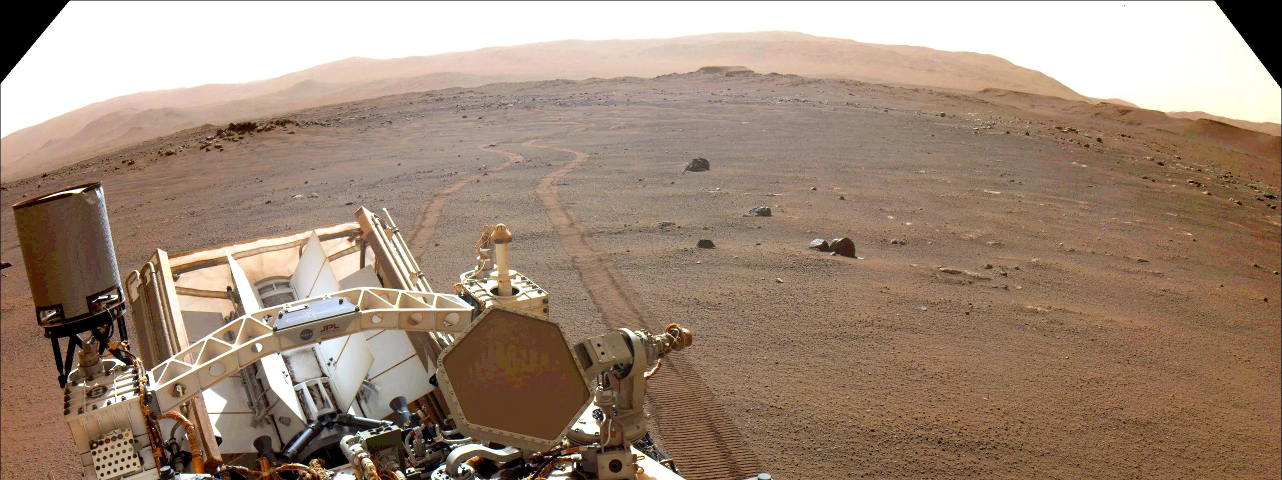 Perseverance rover hardware in the foreground with wheel tracks curving across rocky Martian terrain.