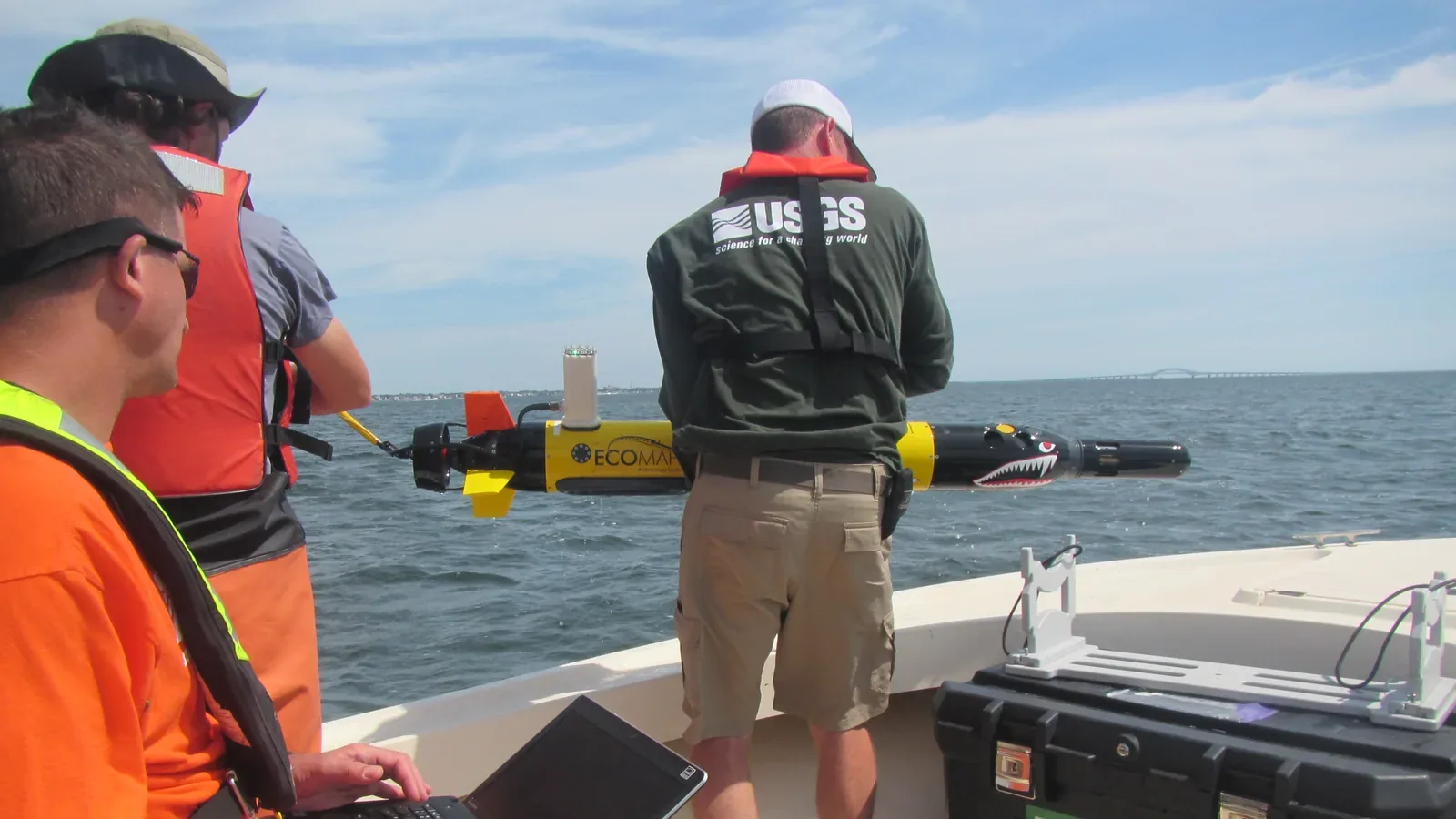 Field crew retrieving a yellow autonomous underwater vehicle beside a research boat.