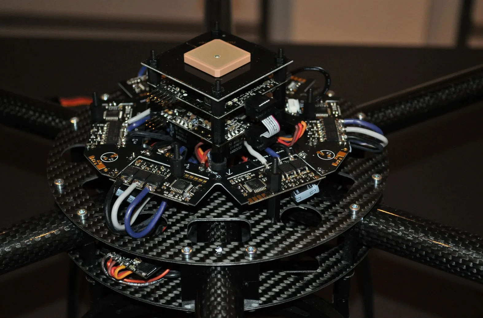 Stacked circuit boards topped by a square GPS antenna, with motor-controller boards and connecting cables arranged around the multicopter frame.