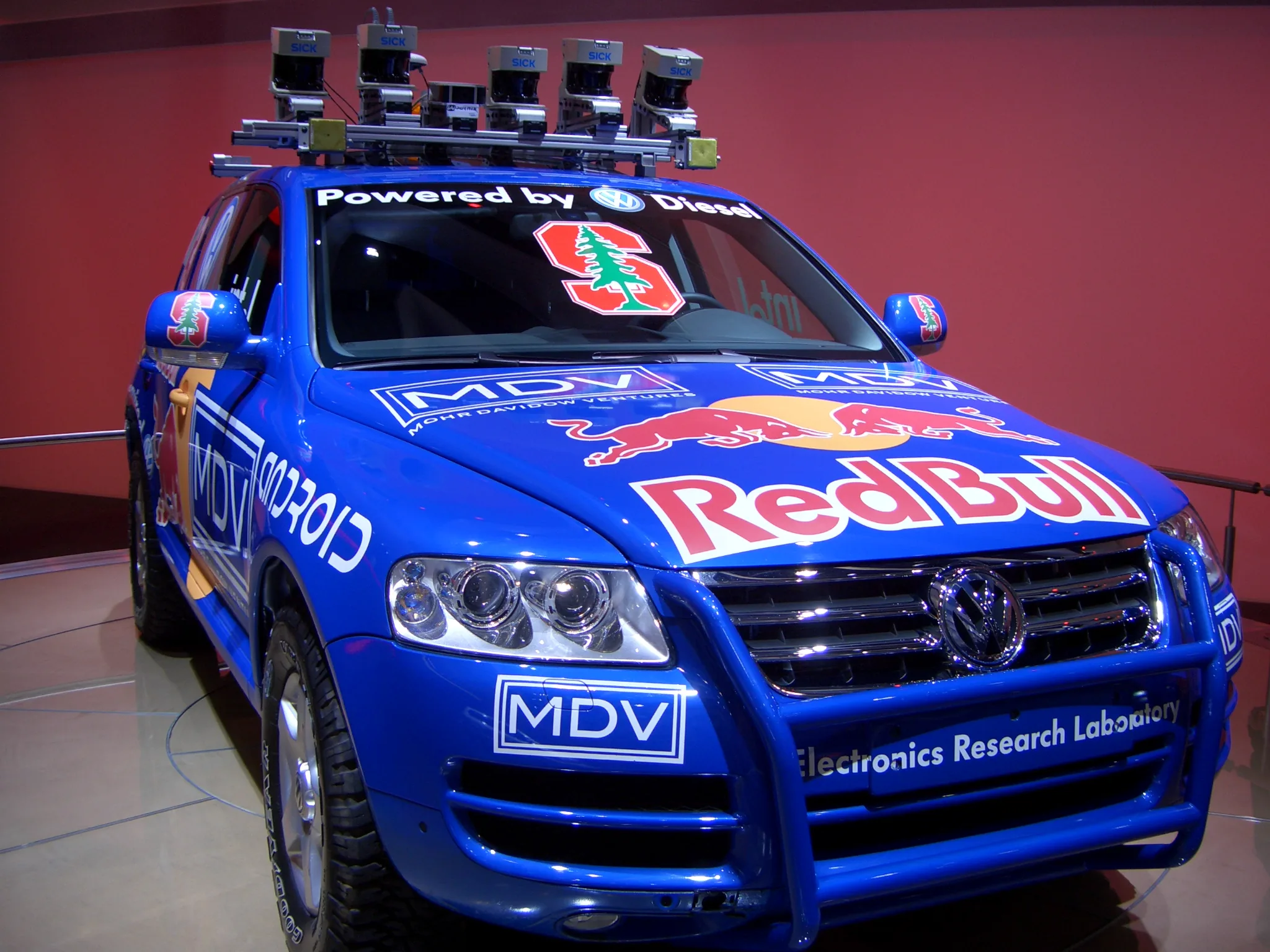 Roof-mounted sensor array on a blue Stanford robotic Volkswagen Touareg displayed indoors.