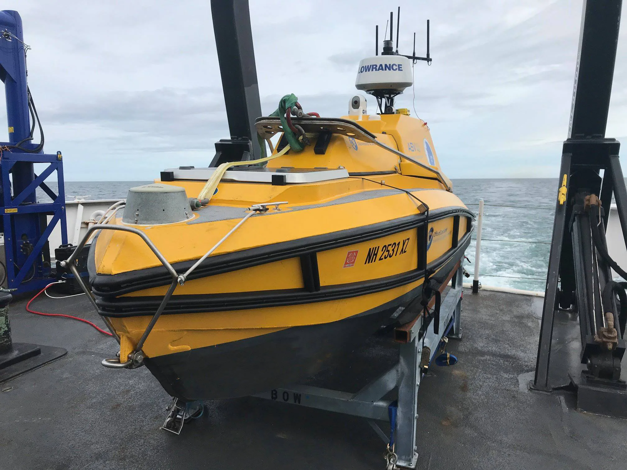 Yellow C-Worker 4 uncrewed surface vessel secured in a shipboard cradle, with antennas, a radar dome, and a camera above the hull