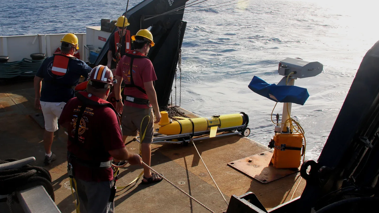 Scientists and ship crew prepare a yellow underwater glider with wings for launch from a research vessel.