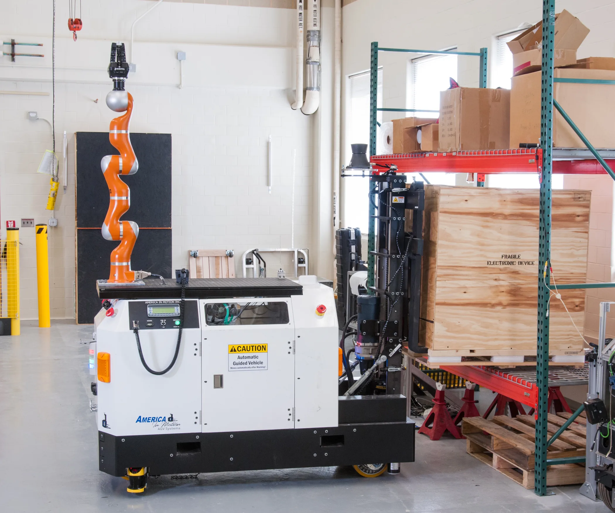 An automated guided vehicle with a fork mechanism beside a wooden crate on industrial shelving in a NIST laboratory.